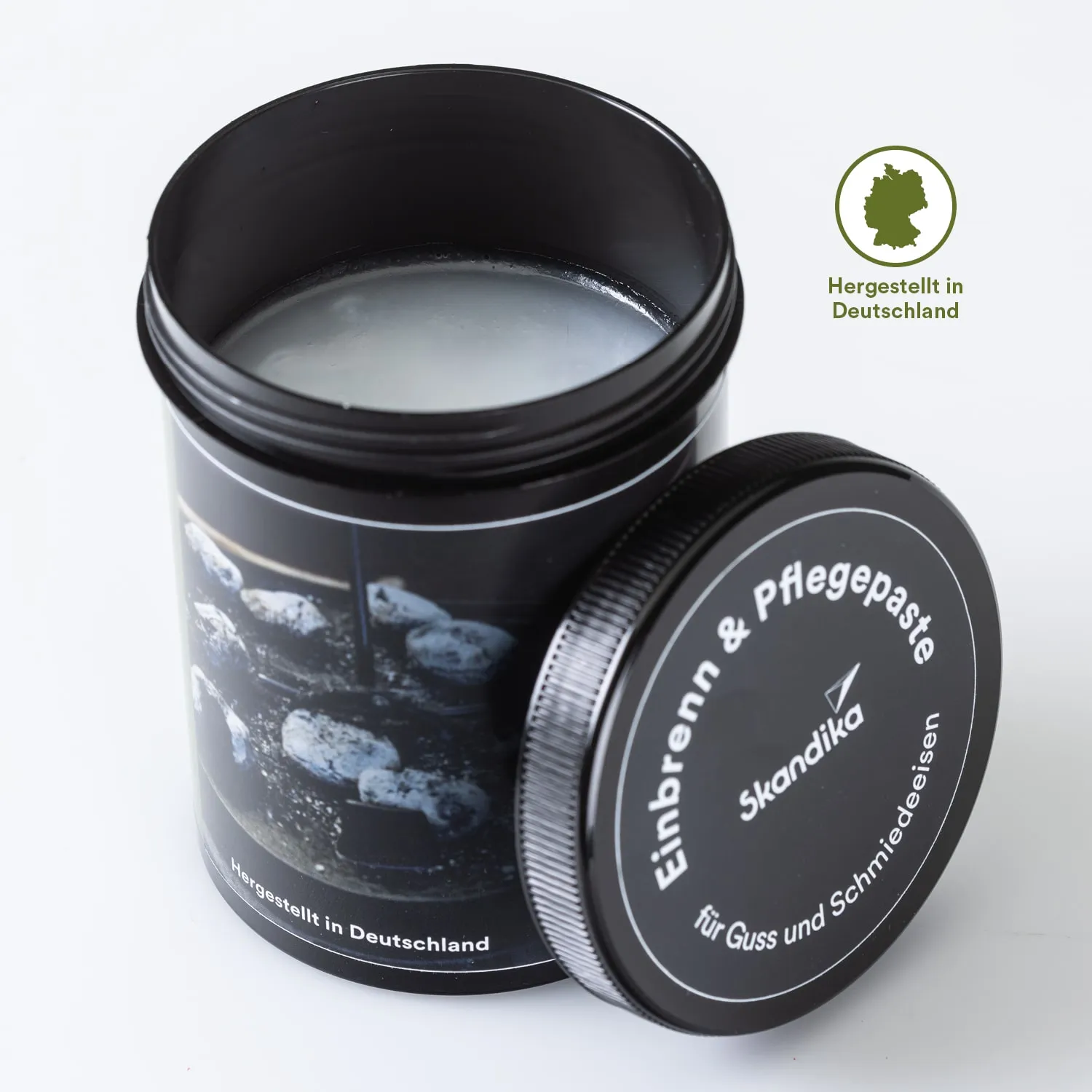 Dose mit Einbrenn- und Pflegepaste, halb geöffnet. Deckel liegt daneben. Aufschrift enthält Produkthinweise und Herkunft.