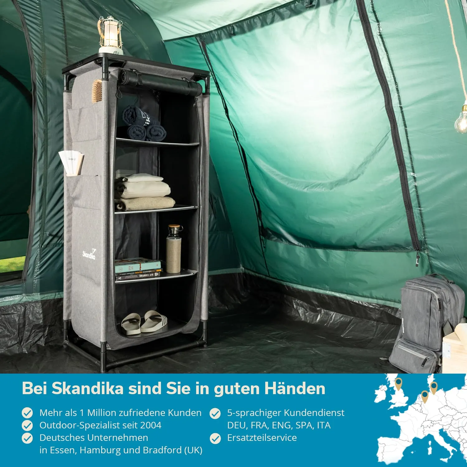 Ein grauer Regalständer steht in einem Zelt und enthält Handtücher, Decken, eine Flasche und Bücher. Eine Laterne ist oben platziert.