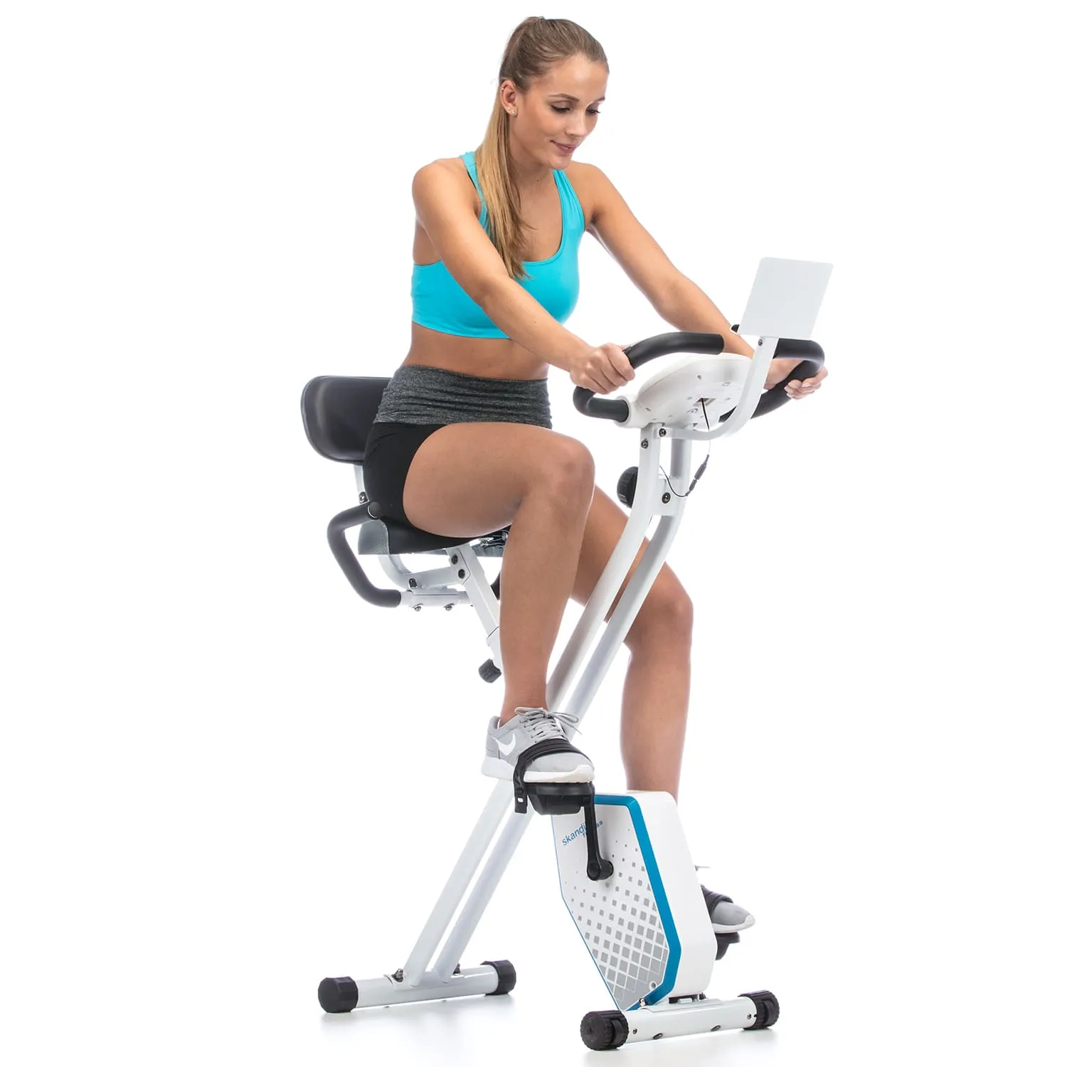 Frau sitzt auf einem Fitness-Bike in blauer Sportoberbekleidung und grauem Shorts, Lenker in Händen haltend.