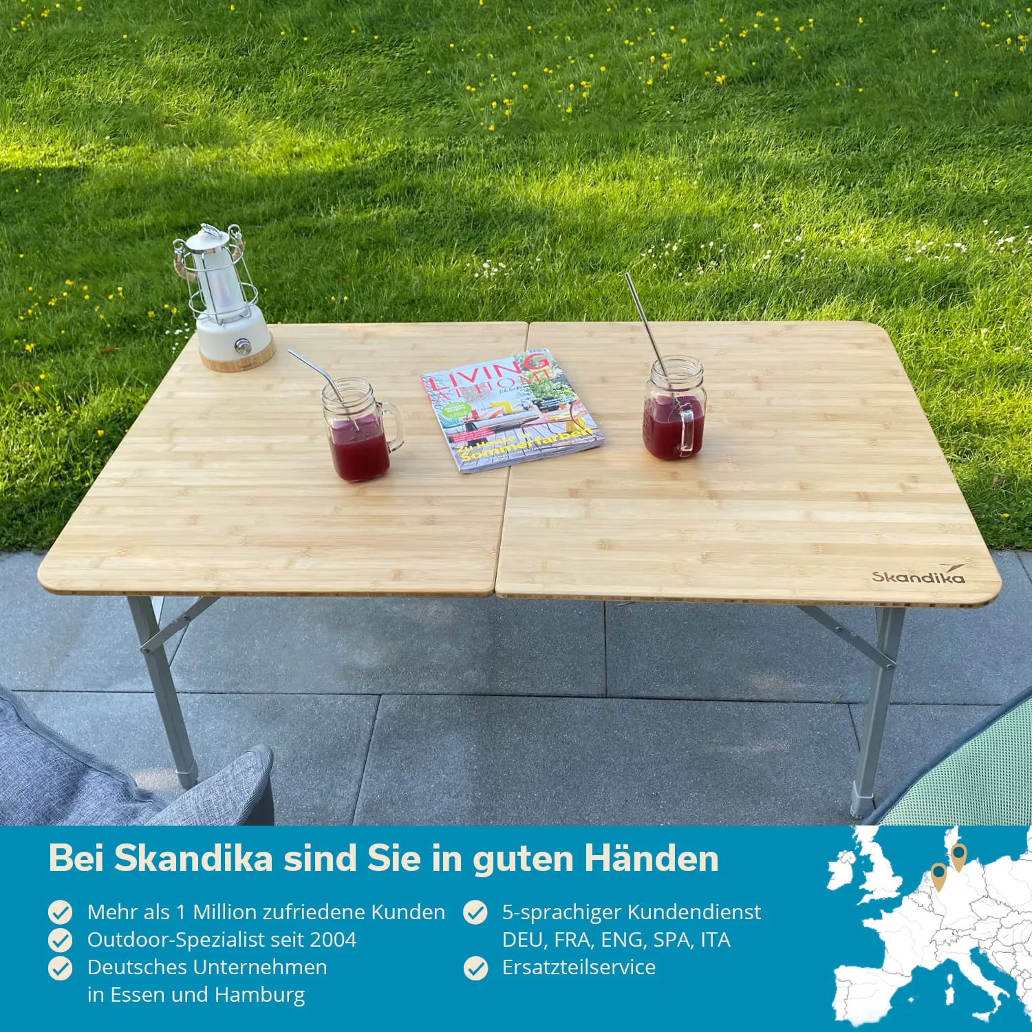 Tisch aus Holz mit zwei Gläsern, einem Magazin und einer Laterne auf grüner Wiese. Stuhl im Hintergrund.