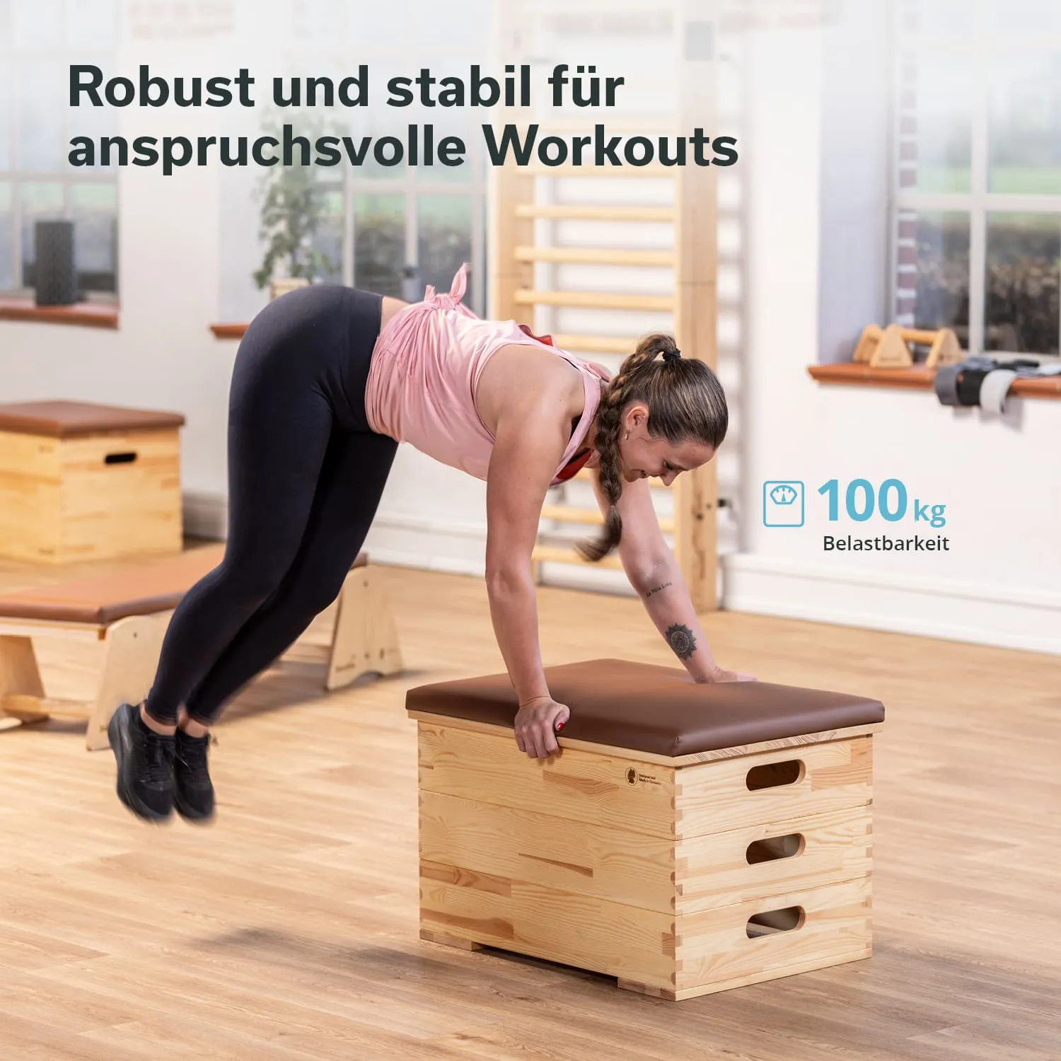 Beige Holzkiste mit brauner Polsterung. Eine Person führt eine Gymnastikübung auf der Kiste aus. Helle Umgebung.