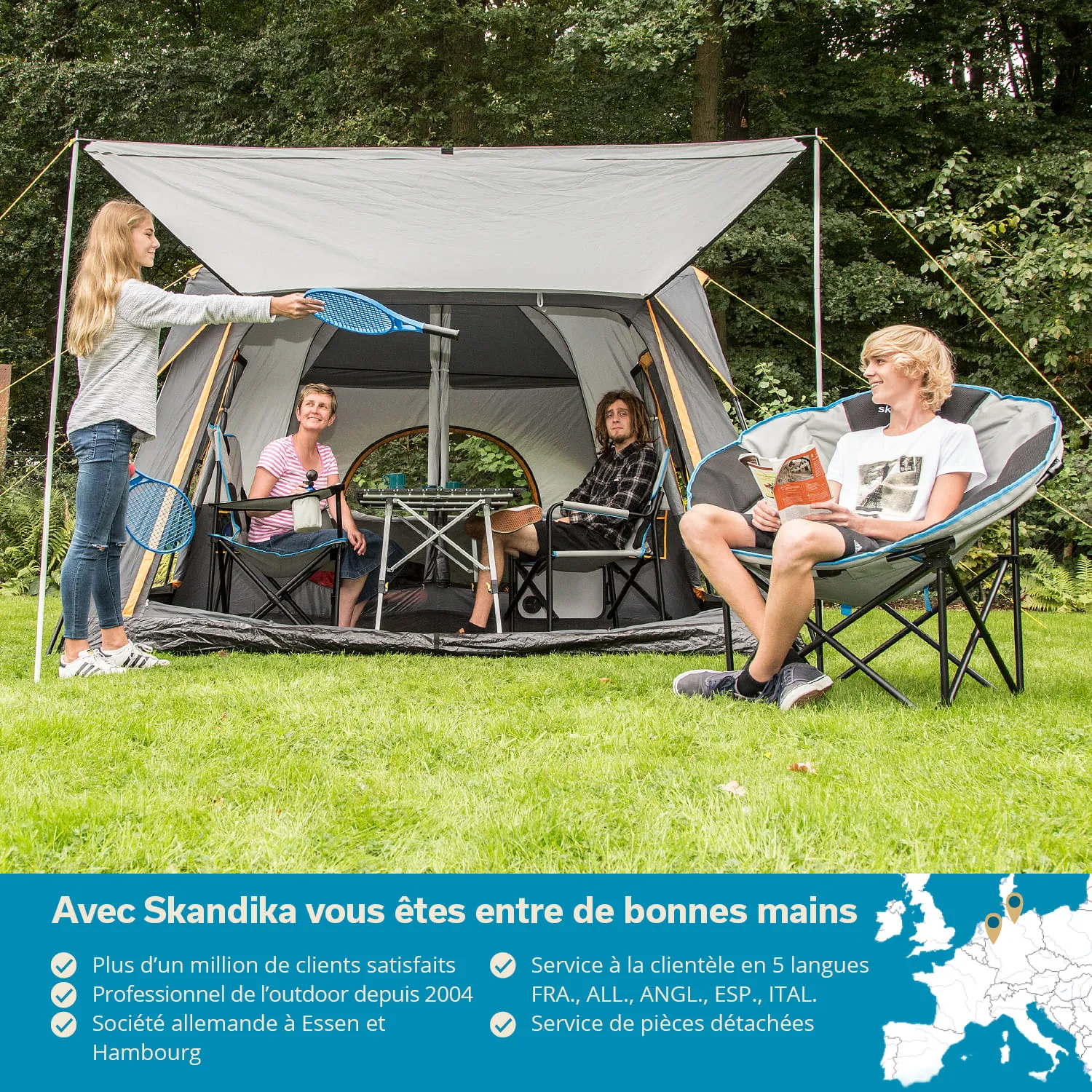 Familie in einem Zelt auf einer Wiese, zwei Personen sitzen, eine Person liest, eine Person steht mit einem Schläger.