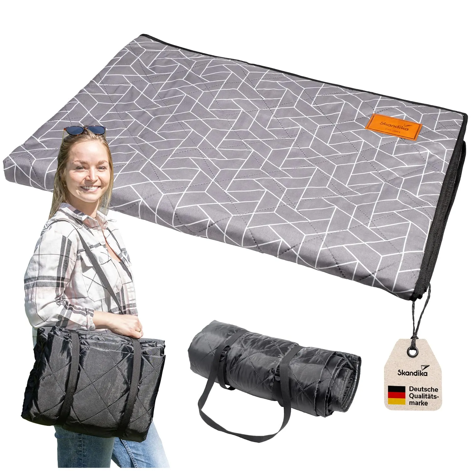 Faltbare Picknickdecke in Grau mit geometrischem Muster, daneben eine Person in kariertem Hemd mit Tasche und gerollte Decke.