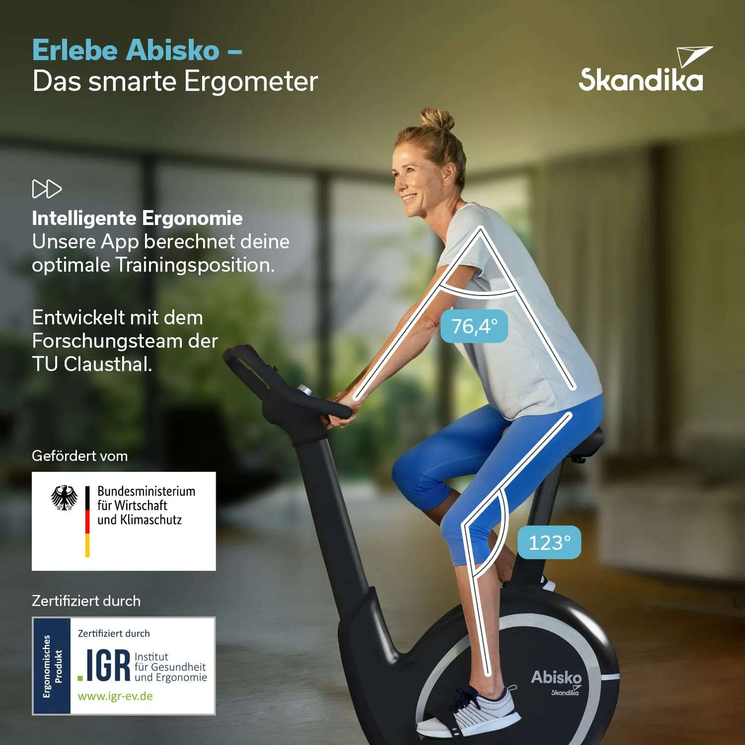 Ergometriegerät in einem hellen Raum, eine Person sitzt darauf, lächelt und trägt Sportkleidung. Pflanzen im Hintergrund.