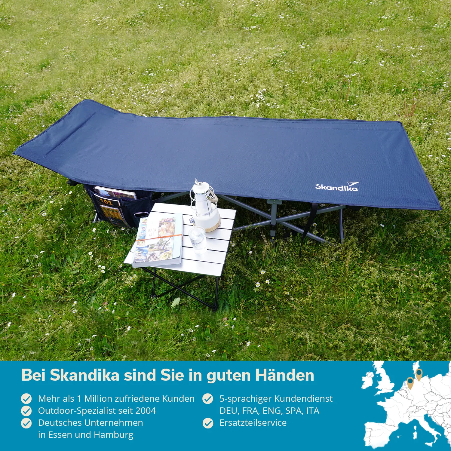 Feld mit grünem Gras, darauf eine Liege in Blau und ein kleiner Klapptisch. Auf dem Tisch stehen eine Lampe, ein Glas und Zeitschriften.