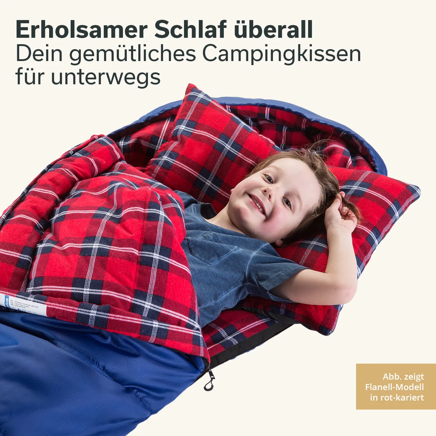 Ein Kind liegt lächelnd in einem Schlafsack mit rot-karierter Decke und Kissen. Der Schlafsack ist blau.