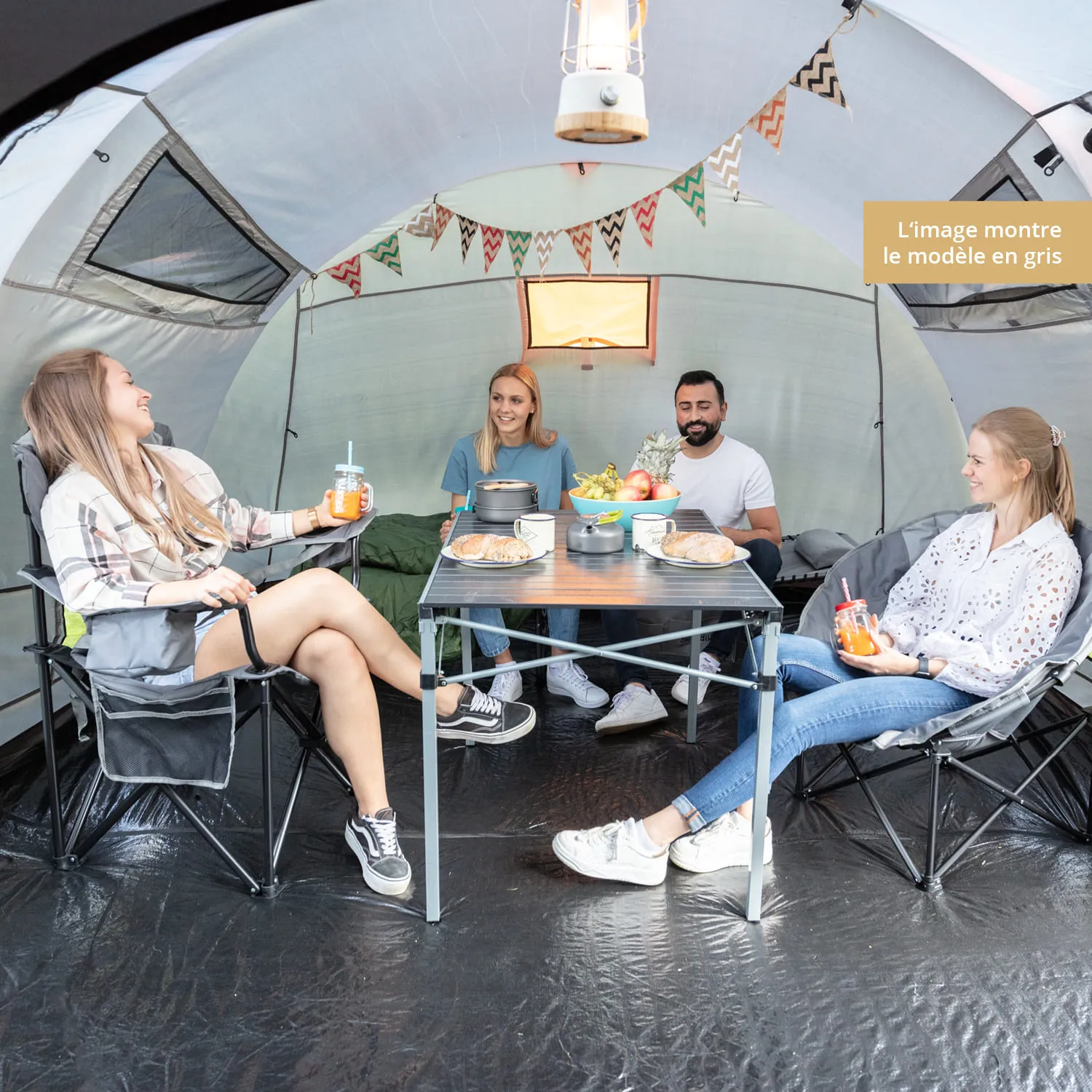 Vier Personen sitzen in einem Zelt um einen Tisch. Auf dem Tisch stehen Lebensmittel und Getränke. Im Hintergrund sieht man eine Girlande.