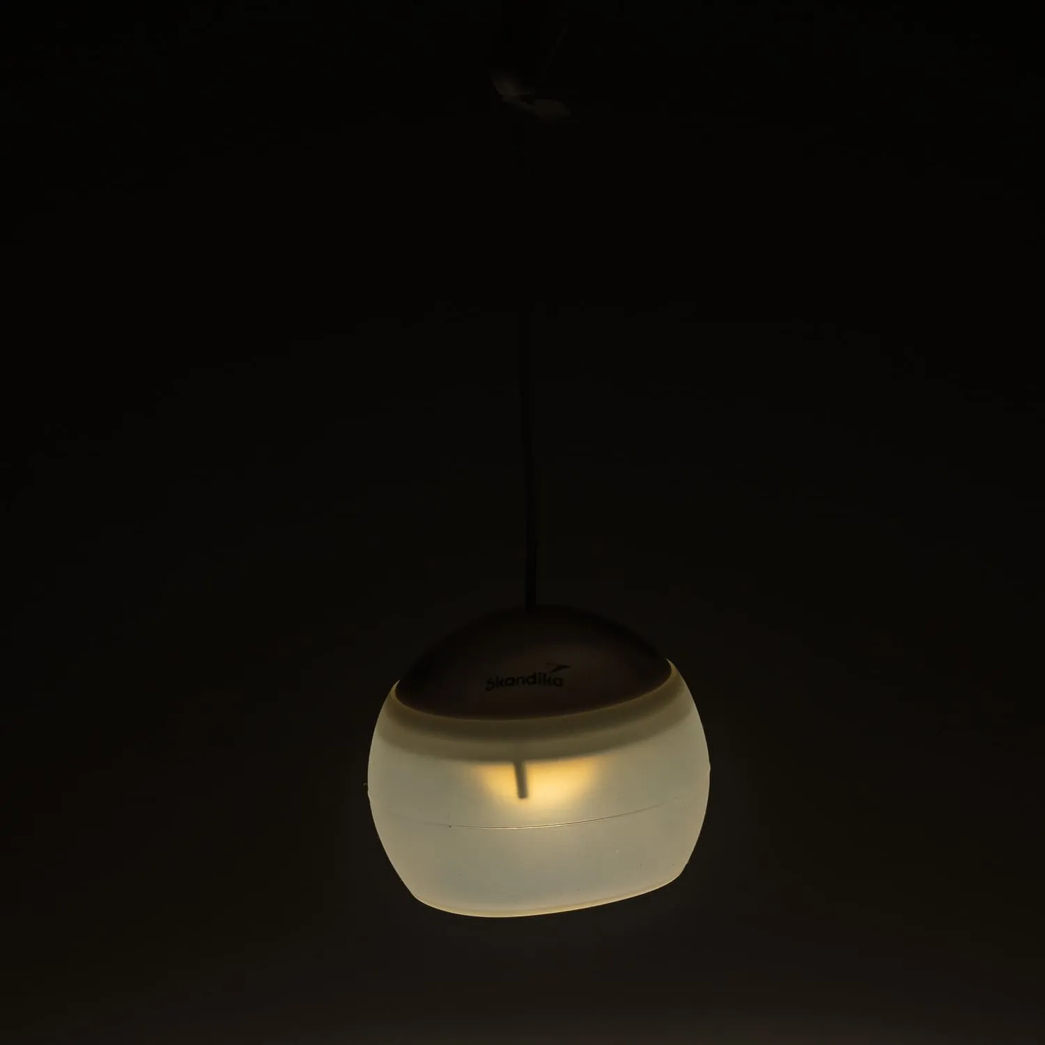 Hängende Lampe mit mattem, ovalem Schirm und schwachem Licht in dunkler Umgebung. Oben mit einem Kabel verbunden.