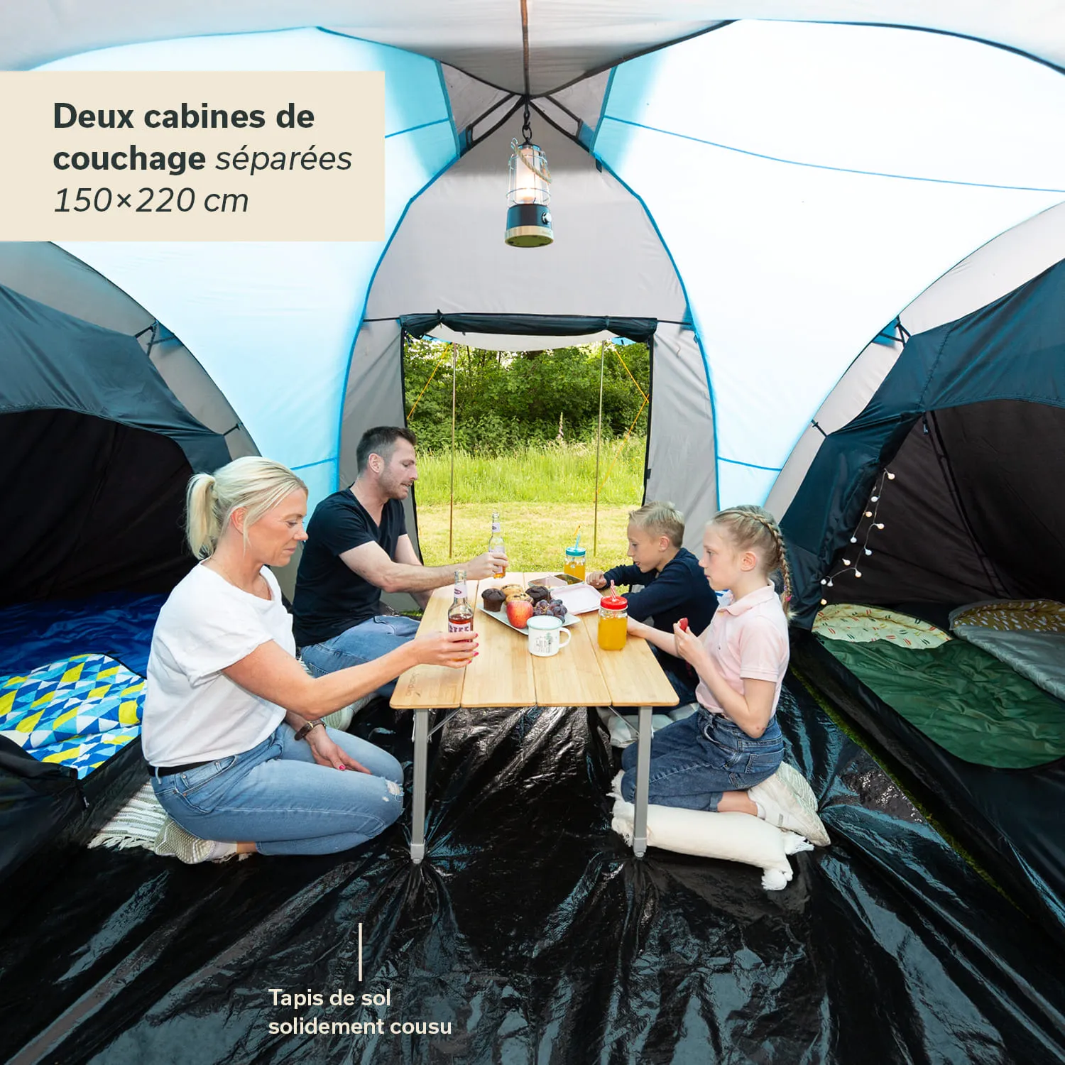 Familie sitzt in einem Zelt an einem Tisch, es gibt Getränke und Snacks. Zwei Schlafkabinen sind sichtbar.
