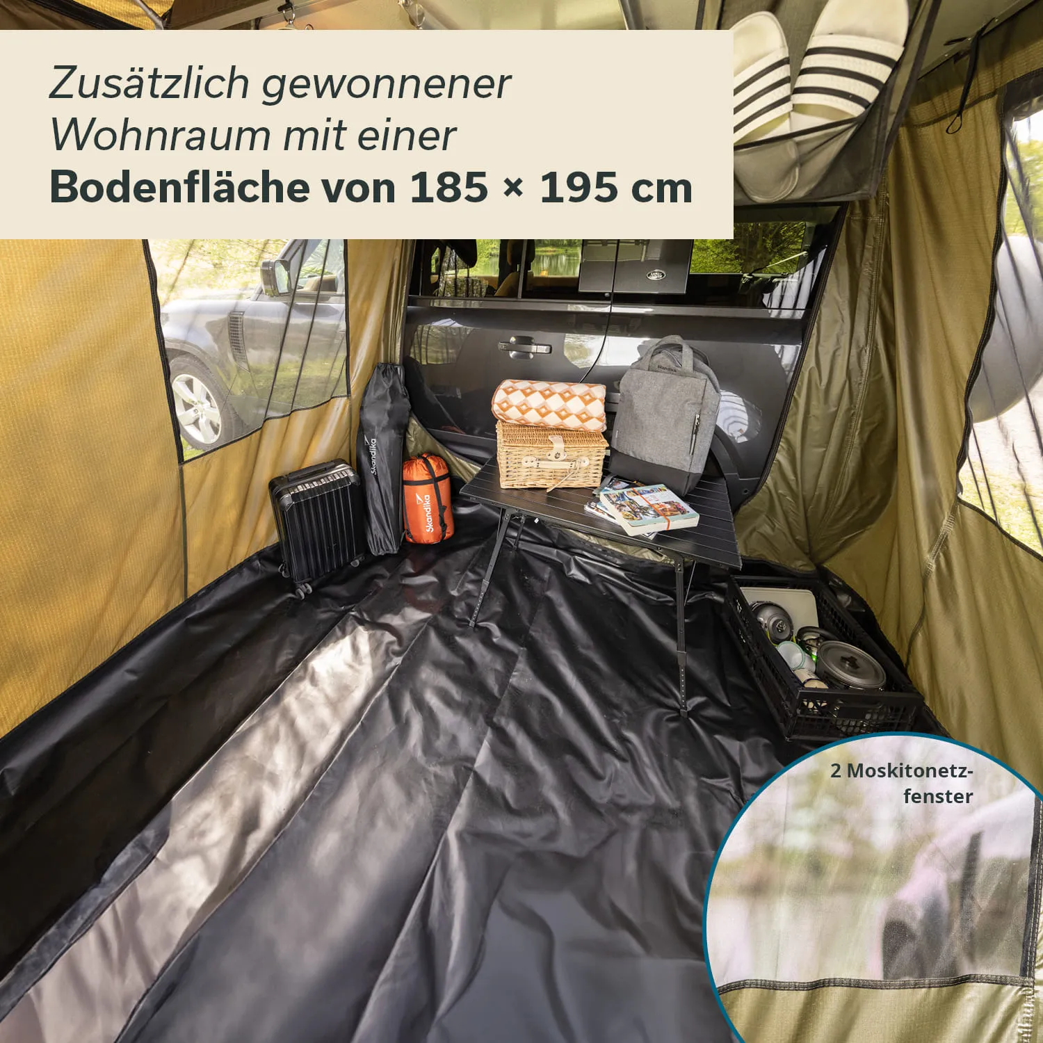 Innenraum eines Vorzeltes, ausgestattet mit einem Tisch, Rucksäcken und einer Picknickdecke. Zweisichtige Fenster sichtbar.
