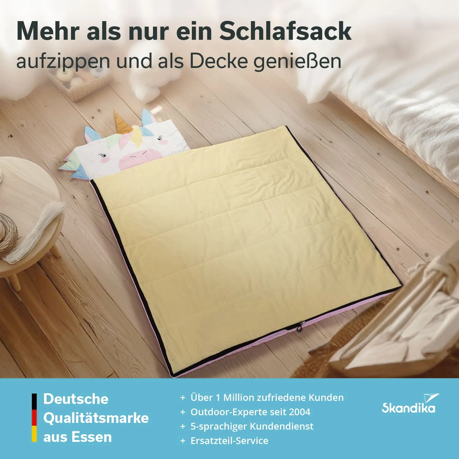 Ein gelber Schlafsack liegt auf einem Holzfußboden, zusätzlich mit einer Decke in Einhorn-Design. Im Hintergrund sind Möbel sichtbar.