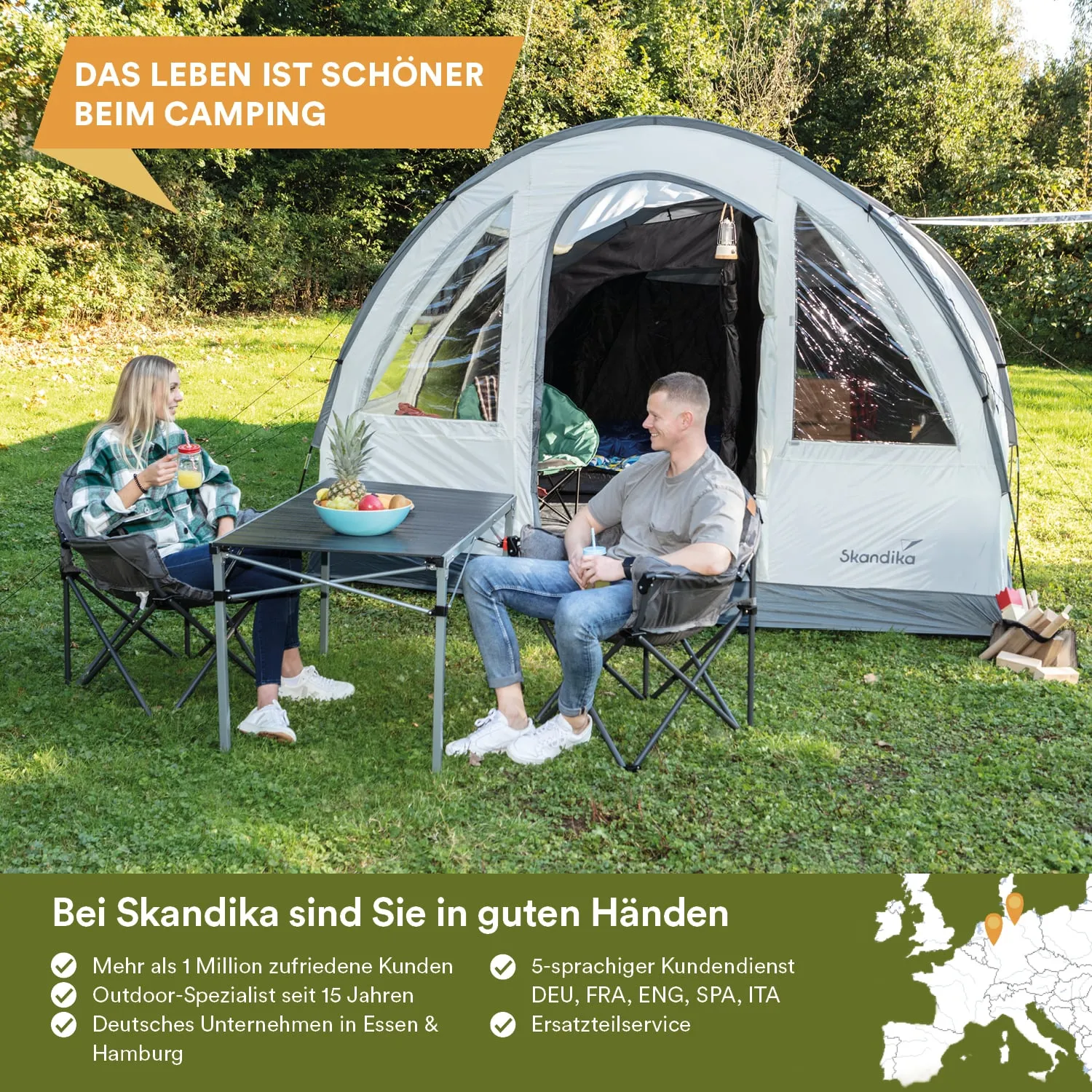 Ein Zelt steht auf einer grünen Wiese. Zwei Personen sitzen an einem Tisch mit Obst und Getränken.