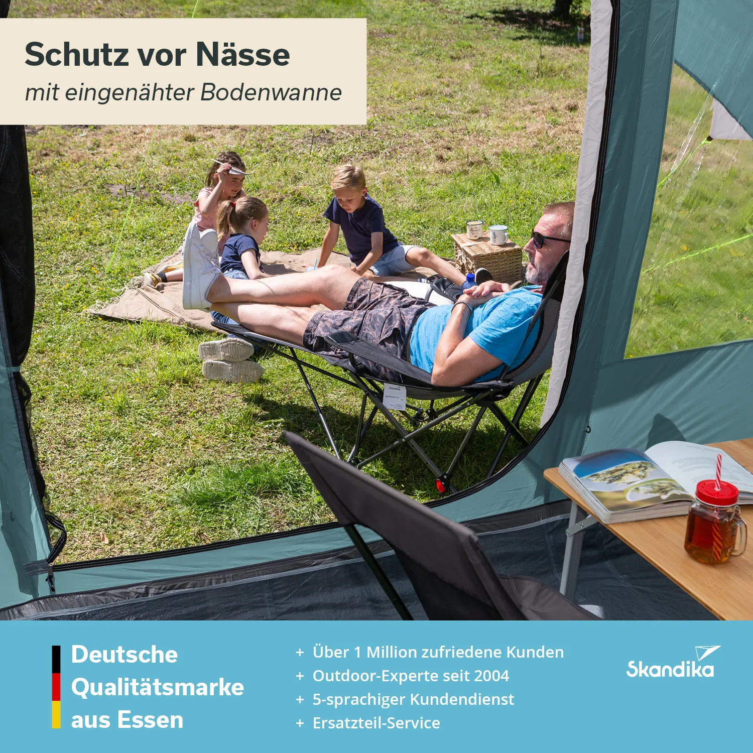 Ein Mann sitzt entspannt in einem Faltstuhl, während zwei Kinder auf einer Decke spielen. Ein Tisch mit Getränken und einem Buch ist im Vordergrund sichtbar.