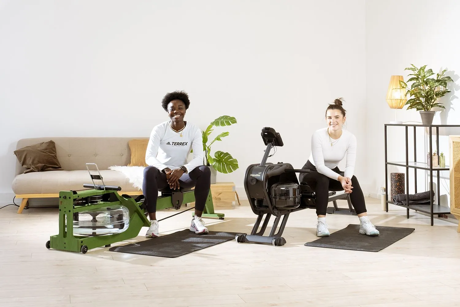 Zwei Sportlerinnen beim gemeinsamen Workout auf zwei Rudergeräten mit Bodenschutzmatte