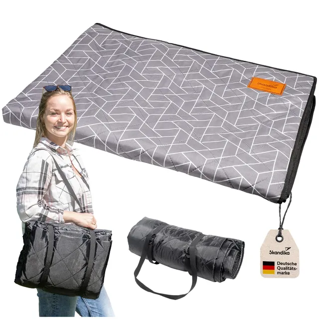 Picknickdecke mit geometrischem Muster, daneben eine Person mit einer Tasche und einer zusammengerollten Decke, Etikett sichtbar.