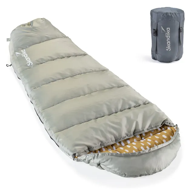 Schlafsack in hellgrüner Farbe, mit gestepptem Design und geöffneter Innenseite in senfgelber Farbe mit weißen Mustern. Rechts ein gepackter Schlafsack in grauer Tragetasche.
