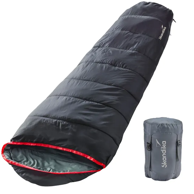 Schlafsack in Schwarz mit roter Innenkante, neben einem grauen Packsack mit Logo.