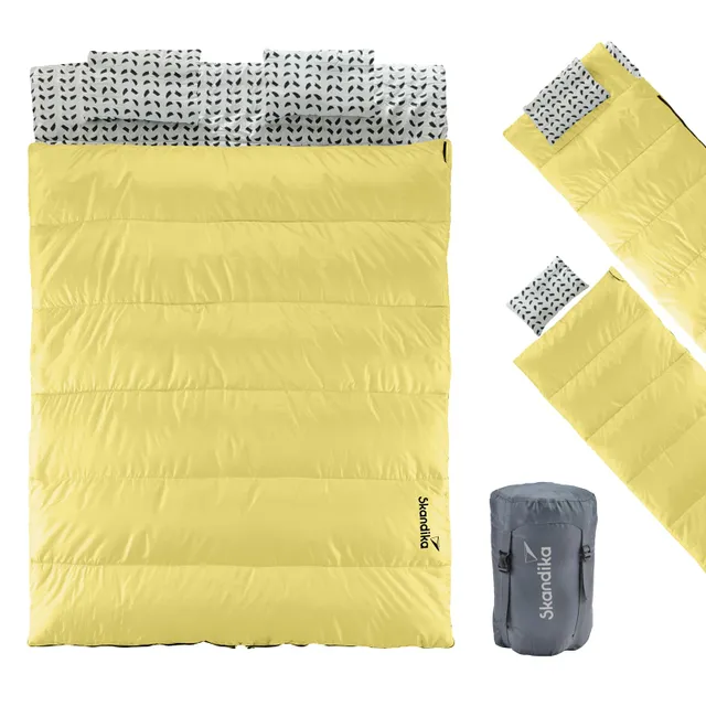 Gelbes Schlafsack-Modell mit weißem, gemustertem Innenfutter und grauer Tragetasche. Zwei separate Einklappkissen sind enthalten.