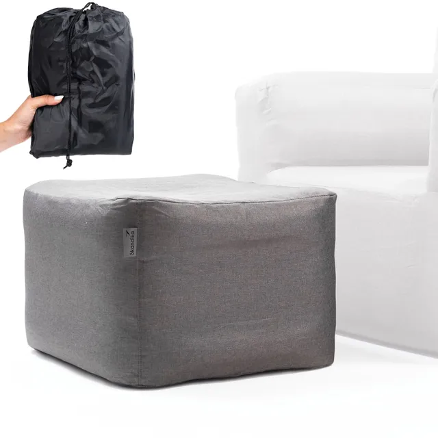 Grauer Pouf neben einem weißen Sessel. Eine Person hält eine schwarze, gefaltete Tasche.