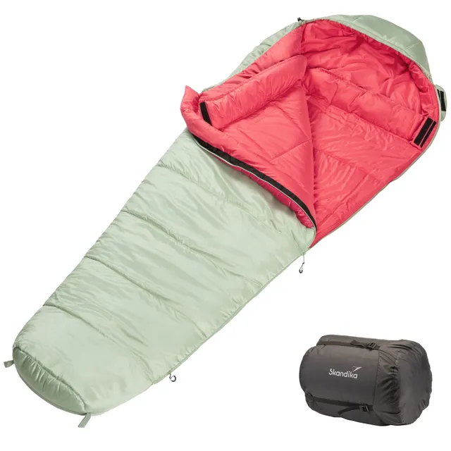 Schlafsack in grüner und roter Farbe, geöffnet und liegend, mit komprimierter Tragetasche daneben.