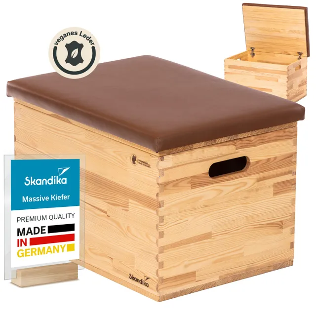 Holztruhe mit braunem, veganem Lederpolster oben. Neben der Truhe kleiner, offener Kasten aus demselben Holz.