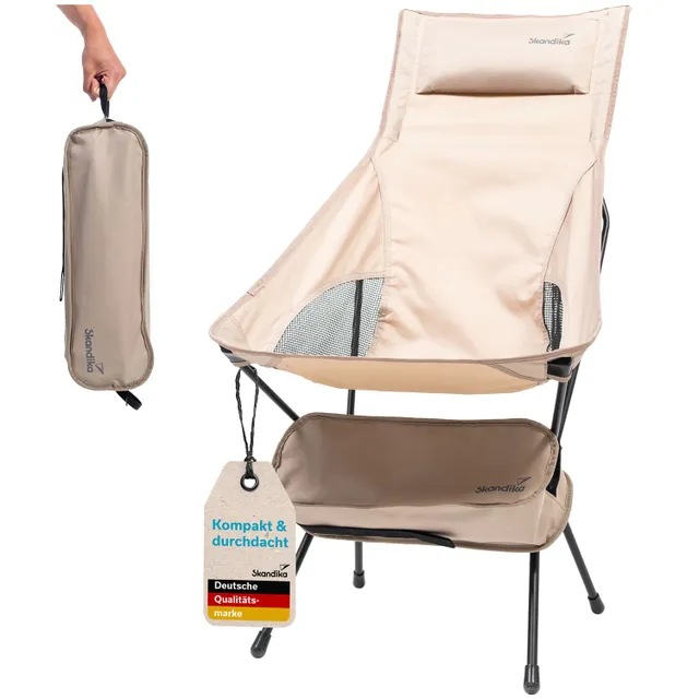 Beige Campingstuhl mit einem Kissen, Handgriff und Unterlage. Im Hintergrund eine Transporttasche. An einem Etikett steht "Kompakt & durchdacht".