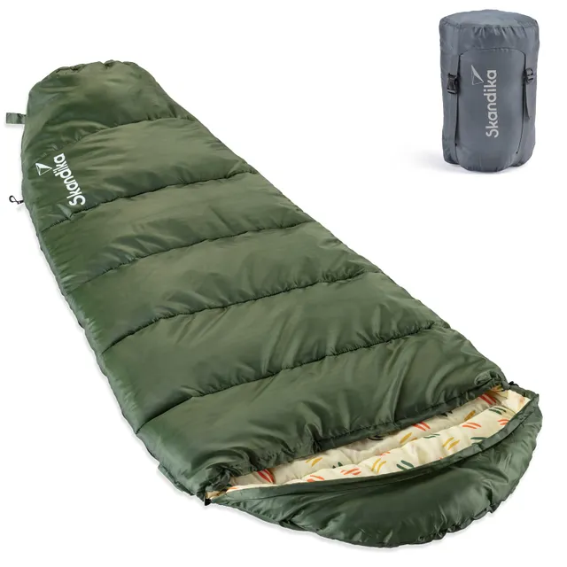 Grüner Schlafsack mit gestepptem Design und geöffnetem Reißverschluss. Neben dem Schlafsack steht ein grauer Kompressionssack.