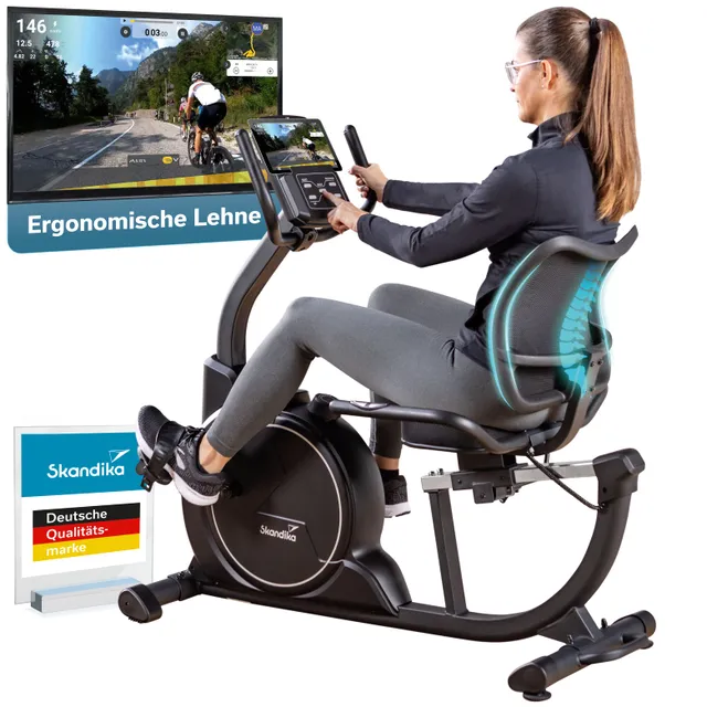 Eine Person sitzt auf einem Stationärfahrrad mit ergonomischer Lehne. Im Hintergrund ist ein Bildschirm mit einer Radstrecke zu sehen. Am Fahrrad befindet sich ein Monitor mit Bedienelementen. Ein Qualitätssiegel der Marke Skandika ist ebenfalls sichtbar.