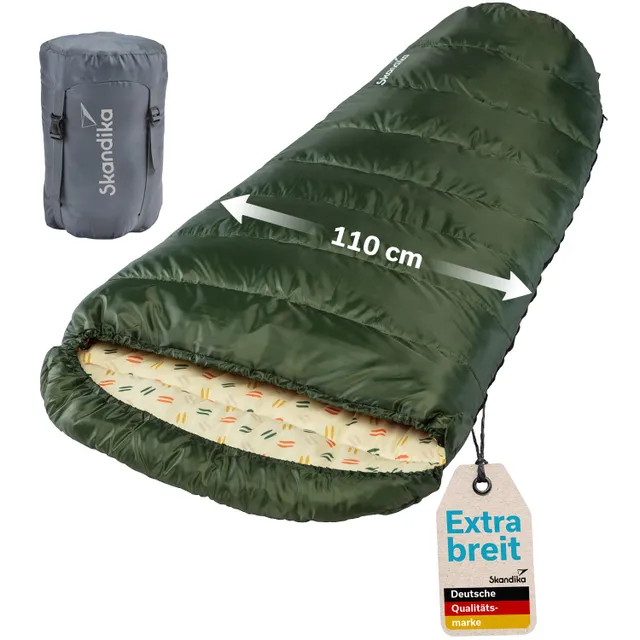 Grüner Schlafsack mit einem breiten Innenraum von 110 cm und buntem Innenfutter. Dazu ein grauer Packbeutel.
