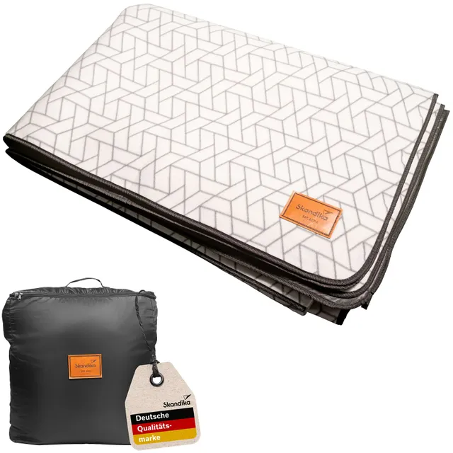 Faltbare Decke mit geometrischem Muster in Grau und Weiß. Dazu ein mit einem Etikett ausgestatteter schwarzer Tragbeutel.