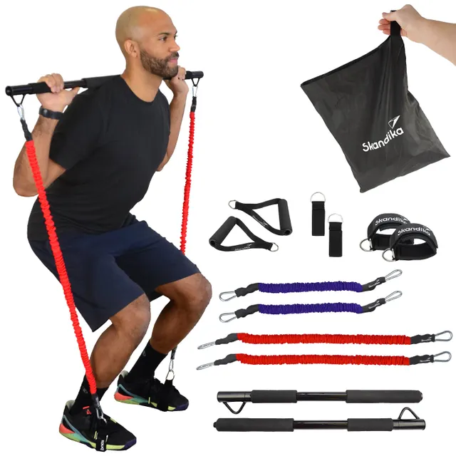 Mann führt eine Kniebeuge mit Widerstandsbändern durch. Um ihn herum liegen Fitnesszubehörteile wie Griffschlaufen und ein Tragetasche.