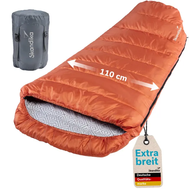 Ein oranger Schlafsack mit einer Breite von 110 cm, daneben ein grauer Packbeutel. Ein Etikett weist auf die Qualität hin.