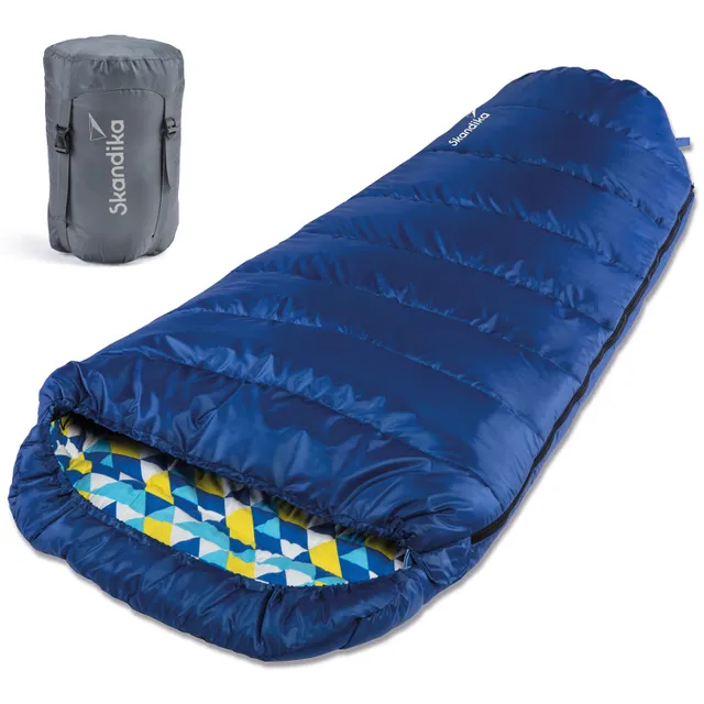 Blauer Schlafsack mit gepolstertem Inneren in geometrischem Muster. Neben dem Schlafsack ein graues, kompaktes Verpackungsbeutel.