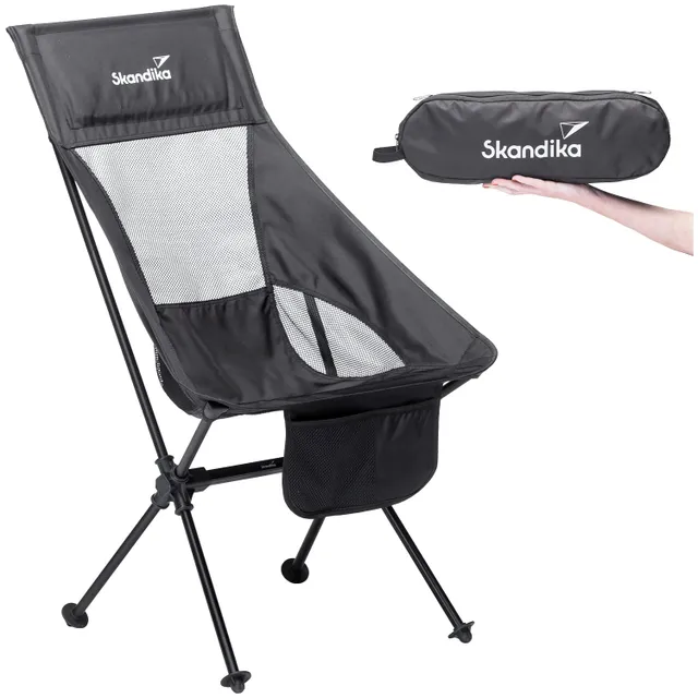 Schwarzer Campingstuhl mit Netzmaterial und einem Stauraum, daneben eine Hand, die eine schwarze Tragetasche hält.