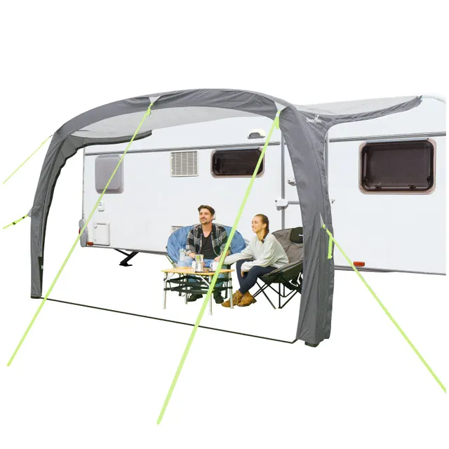 Caravan mit grauem Vorzelt. Zwei Personen sitzen an einem Tisch mit Getränken. Außerdem sind zwei Campingstühle sichtbar.