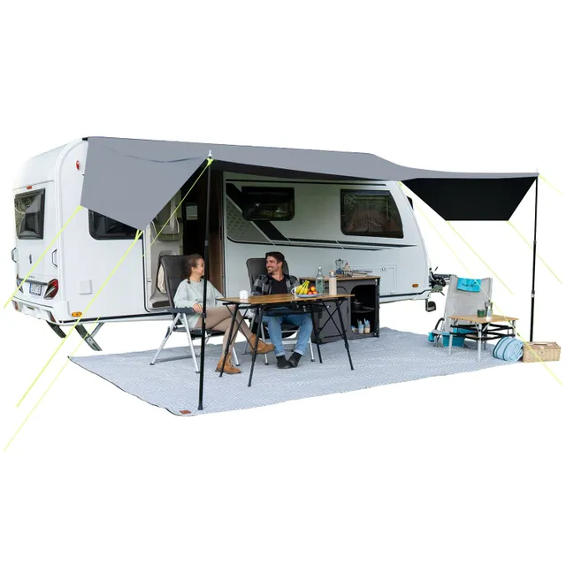 Caravan mit aufgespanntem Sonnenschutz, Tisch mit Getränken und Lebensmitteln, zwei Personen auf Stühlen, Teppich darunter.