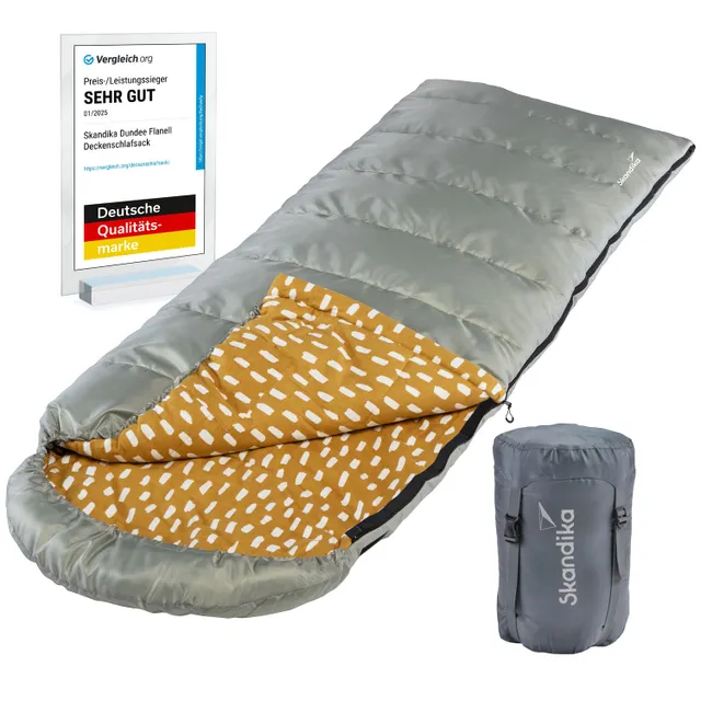 Ein grauer Schlafsack mit einer orangen Innenfläche mit Muster. Daneben steht eine Auszeichnung für "SEHR GUT" von Vergleich.org. Ein komprimierter Beutel ist ebenfalls sichtbar.