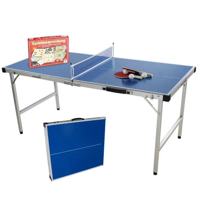 Klappbarer Tischtennistisch mit blauer Tischfläche, Netz, Tischtennisbällen und Schlägern. Eine Spielebox ist im Hintergrund.